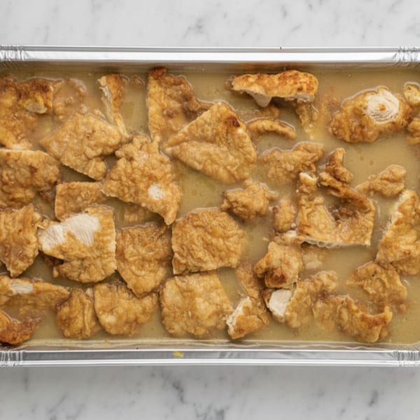 Chicken pieces in a light sauce, served in a large aluminum catering tray.